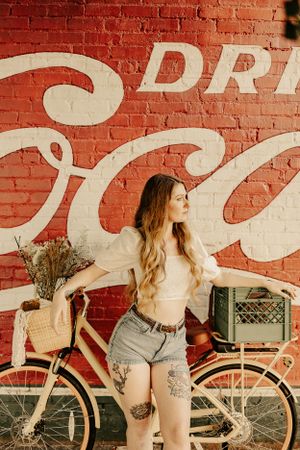 a woman poses on her vintage bike with baskets in front of a large Coca-Cola mural in Western North Carolina near Asheville
