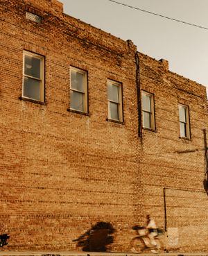 a girl speedily rides her bike along a large brick building in Western North Carolina near Asheville