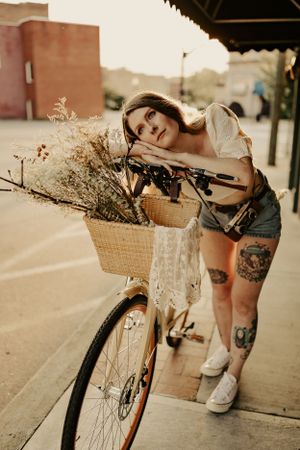 a woman leans on the basket of her bike which is filled with flowers in a downtown setting in Western North Carolina near Asheville