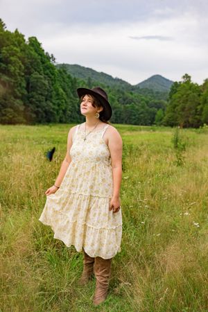 A young woman in a hat and dress stops in a field for a photo and a butterfly flies by in Western North Carolina near Asheville