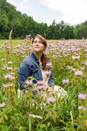 a young lady in a jean jacket sits in a field of flowers in Western North Carolina near Asheville and Cataloochee Valley