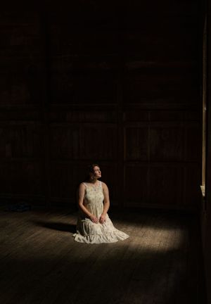 a young lady sits in a dark room illuminated by the light coming through the window in Western North Carolina near Asheville