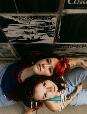 two girls leaning against each others backs and looking up into the camera