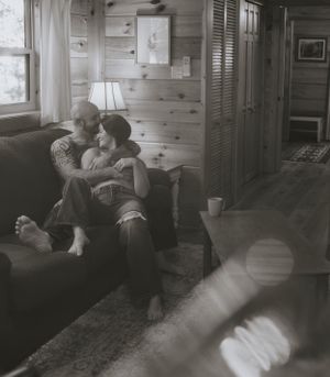 a couple snuggle on the couch of a tiny cabin as light pours in the window in black and white