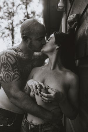 a monochrome shot of a couple sharing an intimate kiss while leaning on the wall holding a cup of coffee in Western North Carolina Asheville