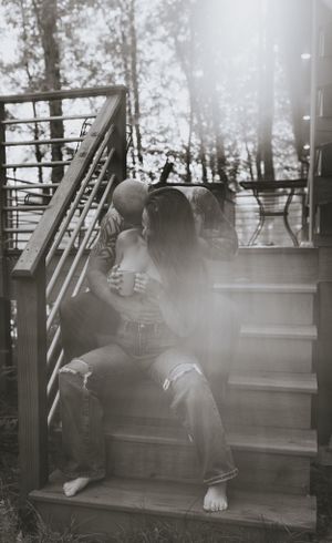 a couple sit on the stairs in an intimate embrace as the sun shines behind them in Western North Carolina near Asheville and Boone