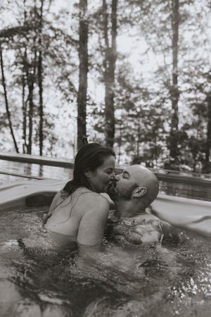 a monochrome photo of a couple sharing a steamy kiss in the hot tub surrounded by woods in Western North Carolina near Asheville and Boone
