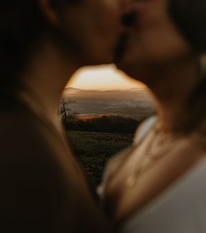 a couple shares a kiss with the sunrise over the mountains in the focus