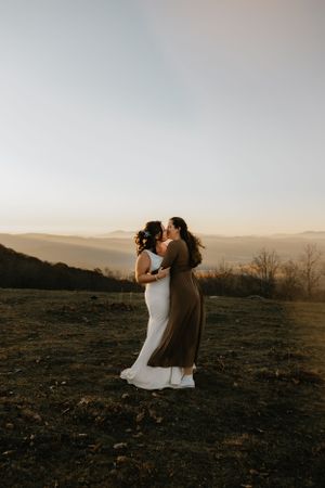 two brides share a kiss in the sunlight on the mountain top