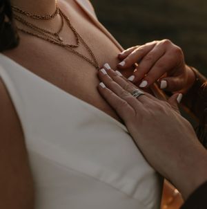 a bride placing her hands on the chest of her partner admiring her gold layered necklace