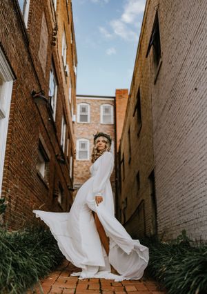 a bride with a earthy crown flips her flowy dress in the alleyway of two brick buildings with blue skies overhead
