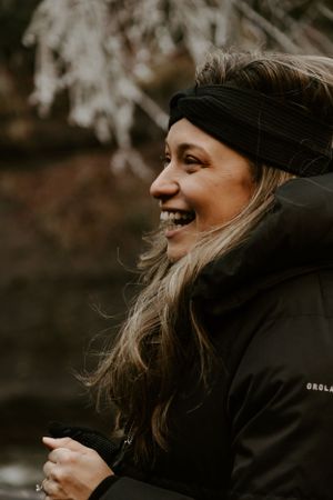 a woman smiles in an all black outfit with ice covered tree limbs in the background