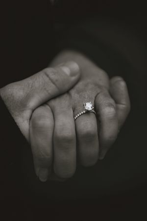 two hands with an engagement ring on the top hand in black and white