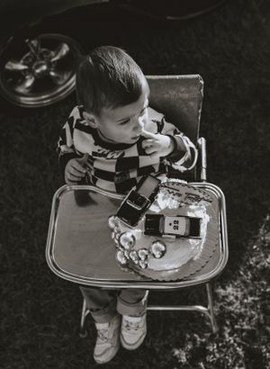 a monochrome shot of a little boy in a vintage highchair with his race car birthday cake and a checkered sweater