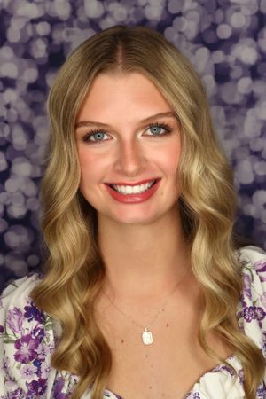 Portrait with wavy blonde hair against purple bokeh background.