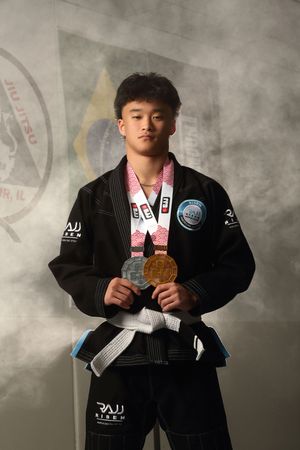 Young martial artist in black BJJ gi proudly displays gold and silver medals at a Brazilian Jiu-Jitsu competition.