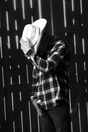Artistic black and white photo of person in plaid shirt and cowboy hat with dramatic lighting effects.