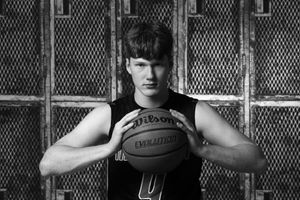Black and white portrait of basketball player holding a Wilson ball against chain link fence wearing a dark tank top.