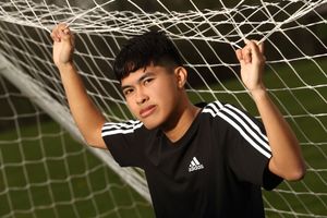 Athletic person in black Adidas shirt poses against soccer goal net during outdoor photo shoot.