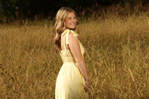 Young blonde woman in yellow sundress smiling over shoulder in golden field.