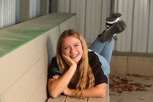 Person with long blonde hair lies casually on wooden floor near autumn leaves.