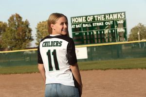 High school softball player throws ball across sunny field during afternoon practice session.