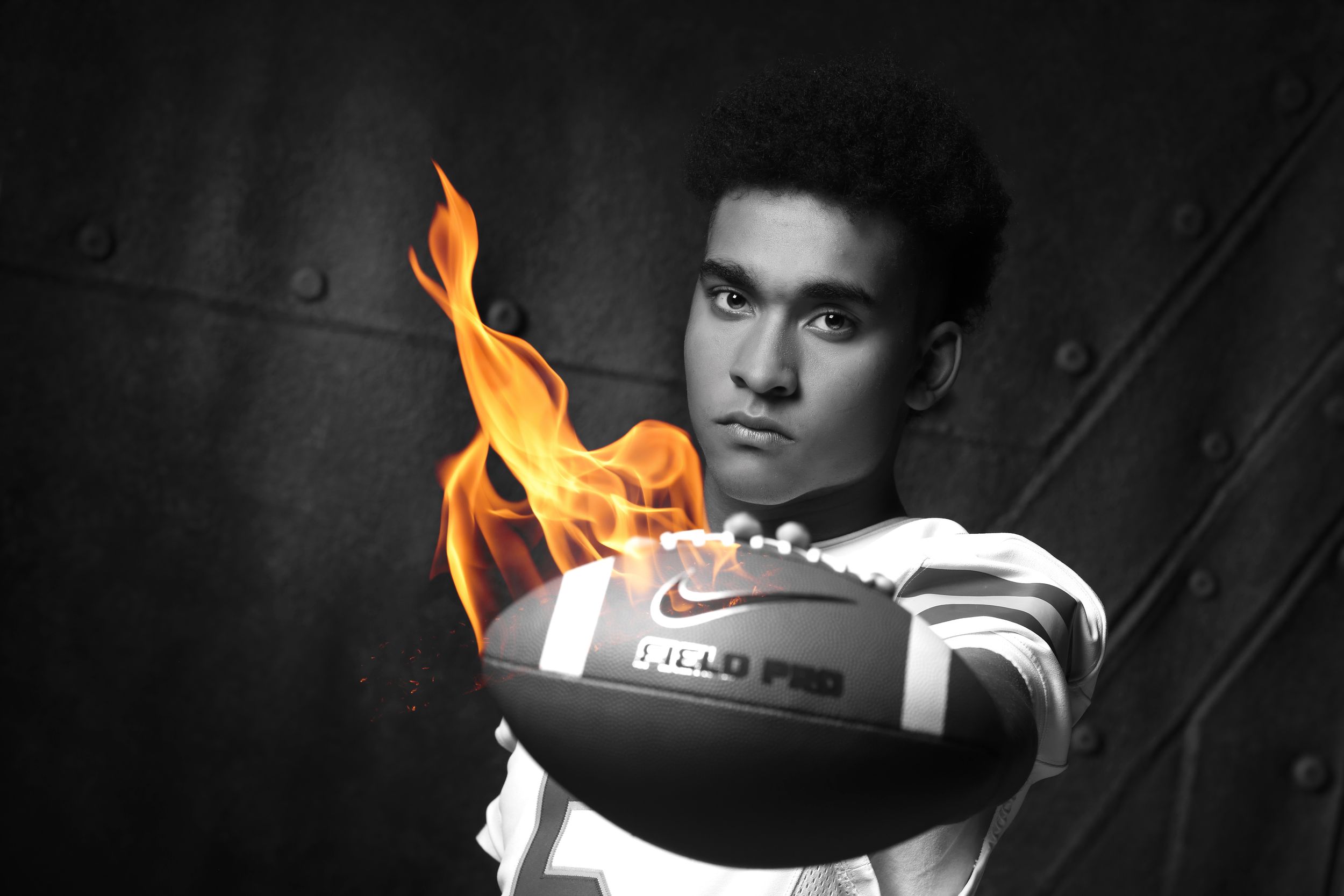 Young athlete holding a flaming Nike football in a dramatic black and white sports portrait photo.