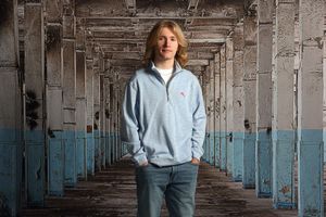 A figure stands centered in a long industrial hallway with blue walls and repeating concrete columns creating perspective.