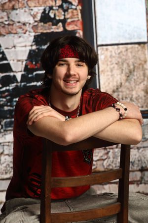 A person wearing a red shirt sits in a wooden chair against a rustic brick wall background.