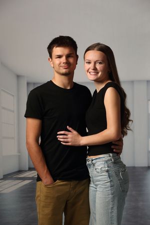 Young couple in black tops smiling together in a bright white room, man in khaki pants and woman in jeans.