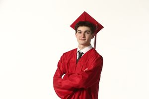 A graduate in a bright red cap and gown stands with arms crossed against a white background.