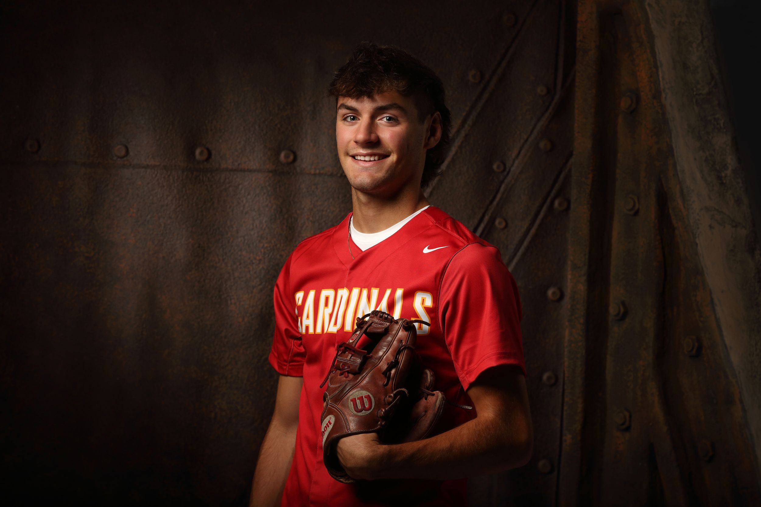 Young baseball player in red Cardinals jersey holding a Wilson glove, posing for a portrait photo.