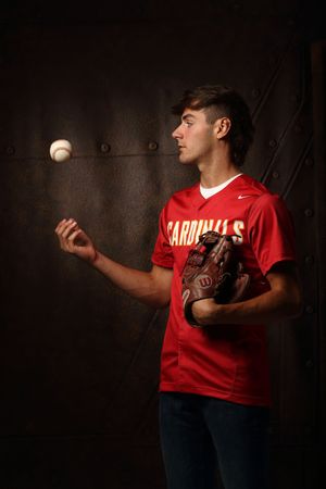 Young baseball player in red Cardinals jersey tossing a ball while holding a Wilson glove indoors.