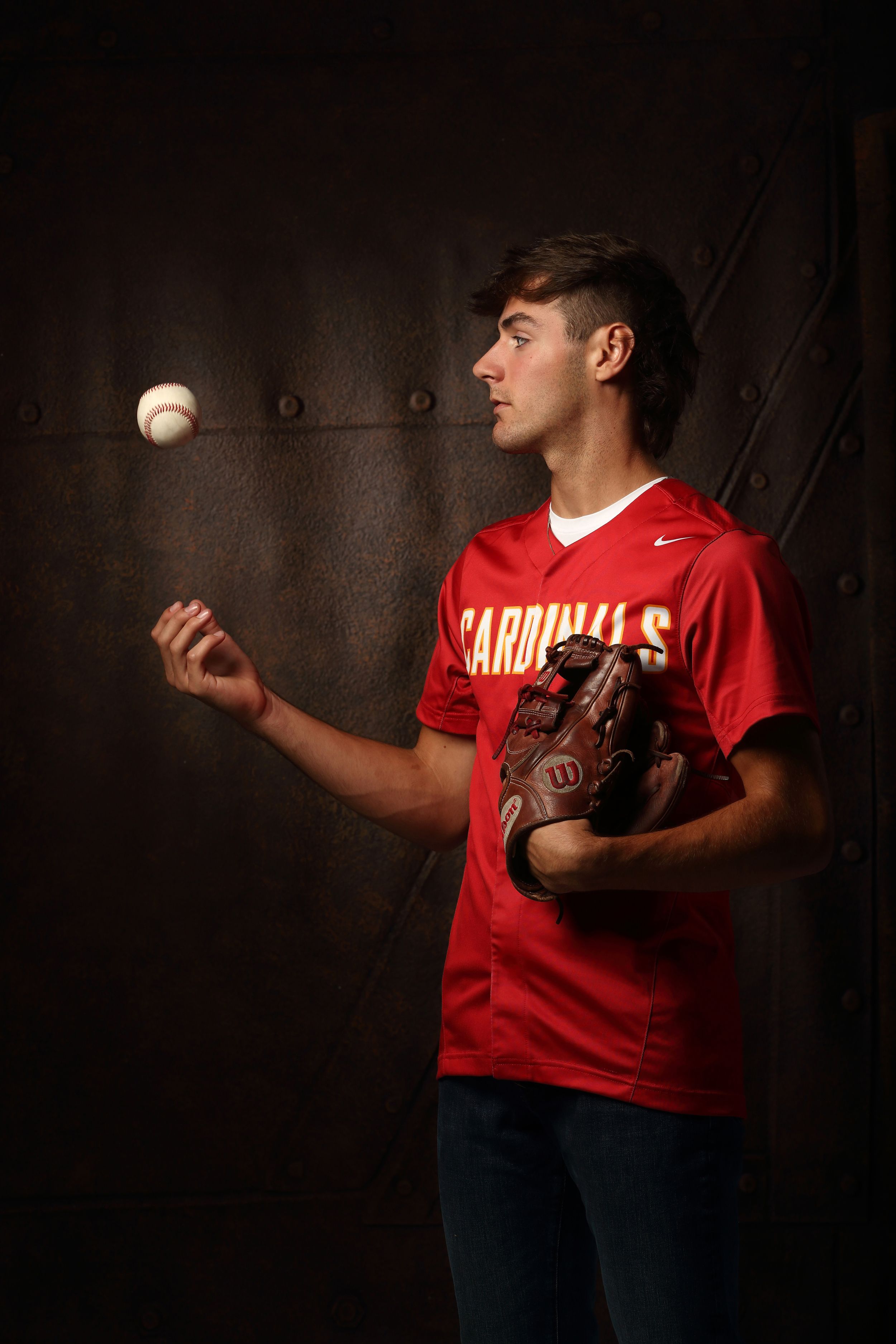 Young baseball player in red Cardinals jersey tossing a ball while holding a Wilson glove indoors.