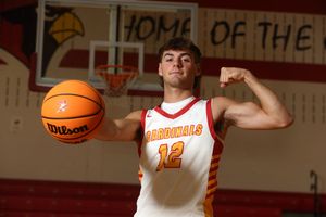 Cardinals #12 basketball player flexing while holding a Wilson ball in a school gymnasium.
