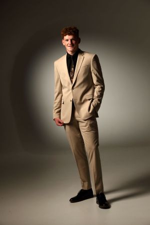Fashion photo of someone in a beige suit against a gray backdrop.