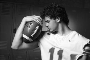 Black and white photo of a young football player in jersey number 11 holding a football against lockers.