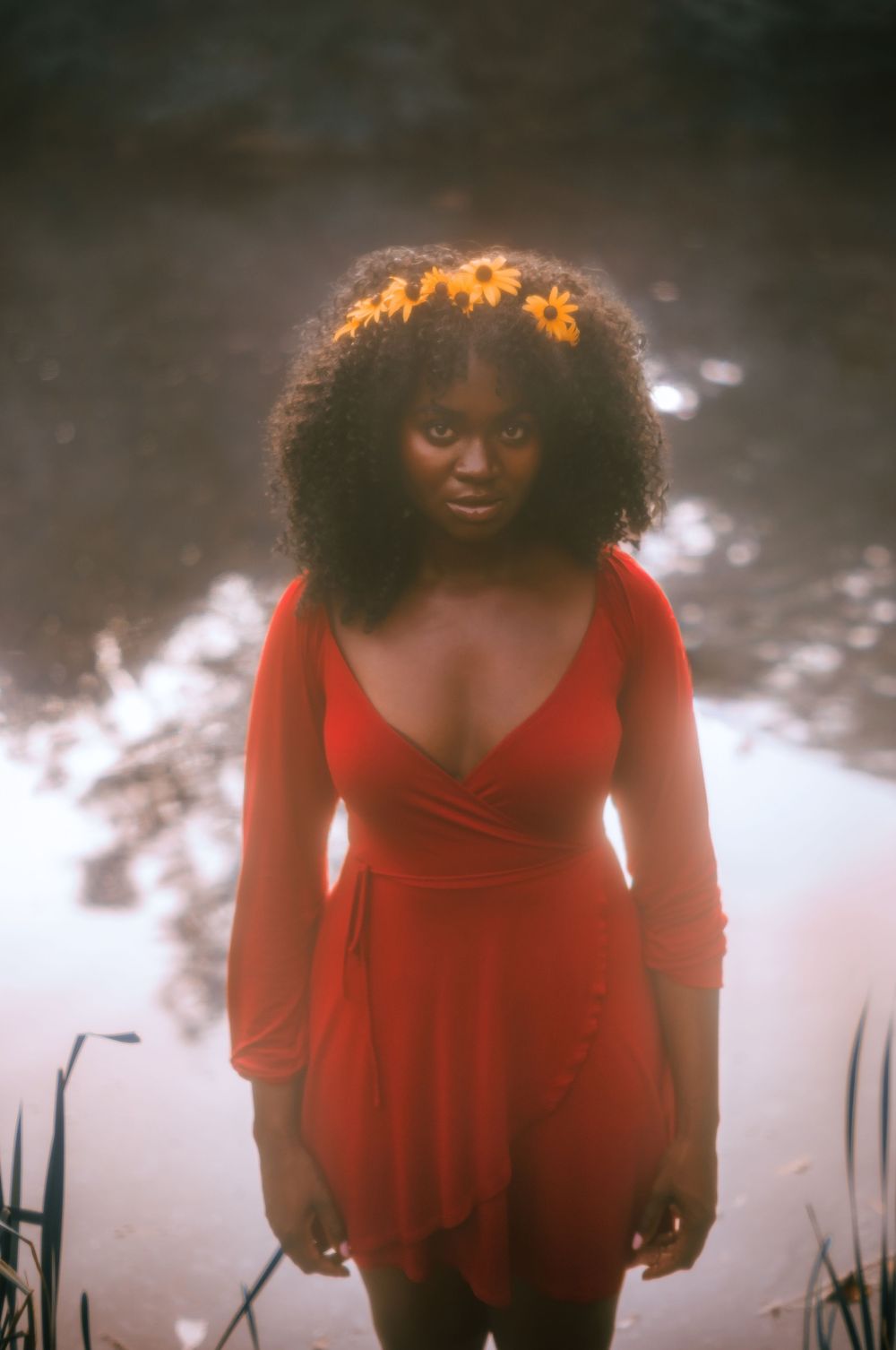 Woman in a flowing red dress poses outdoors in an artistic photoshoot with natural lighting.
