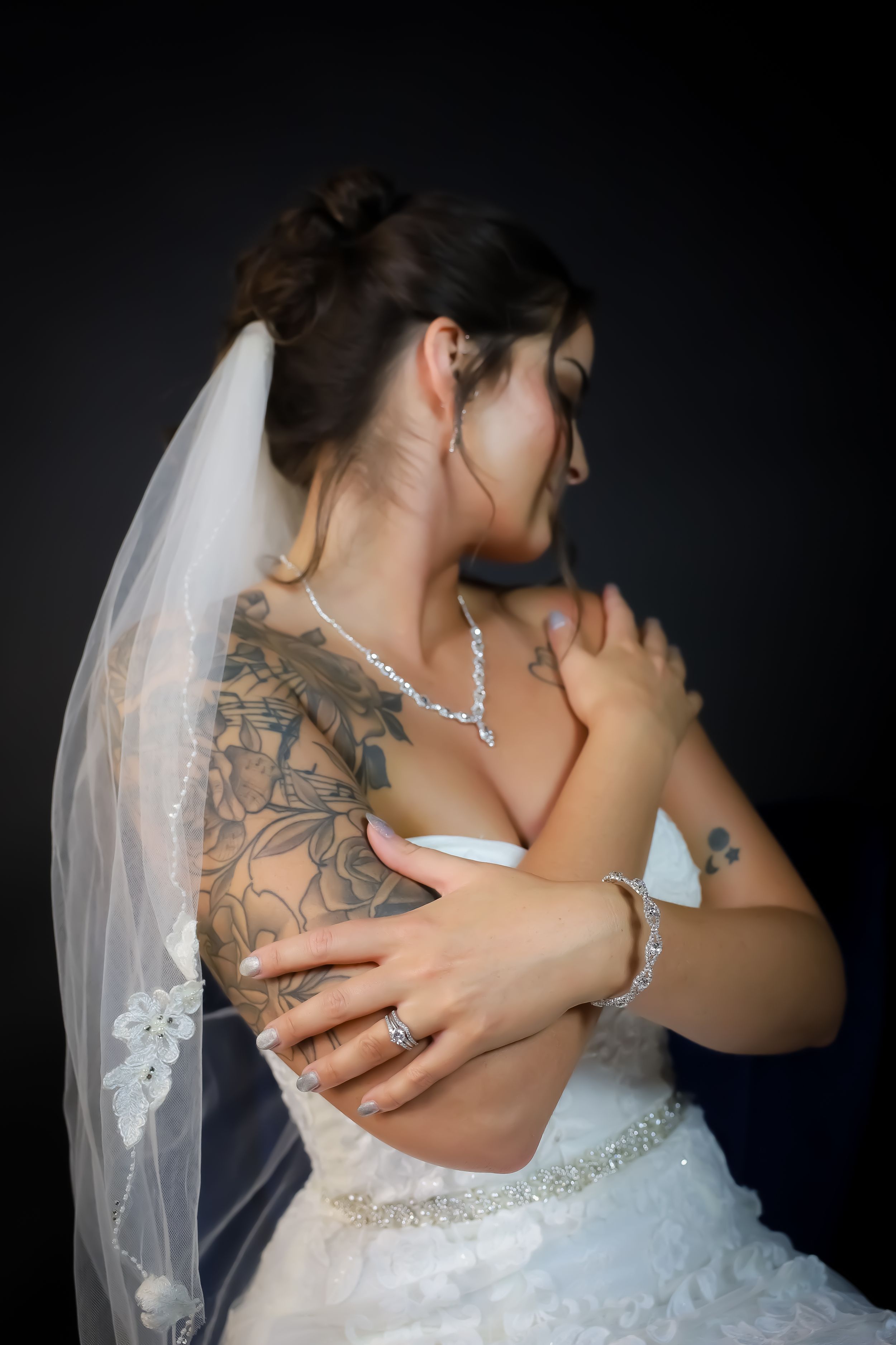 Close-up of bride's tattoos and jewelry with white lace wedding dress details.