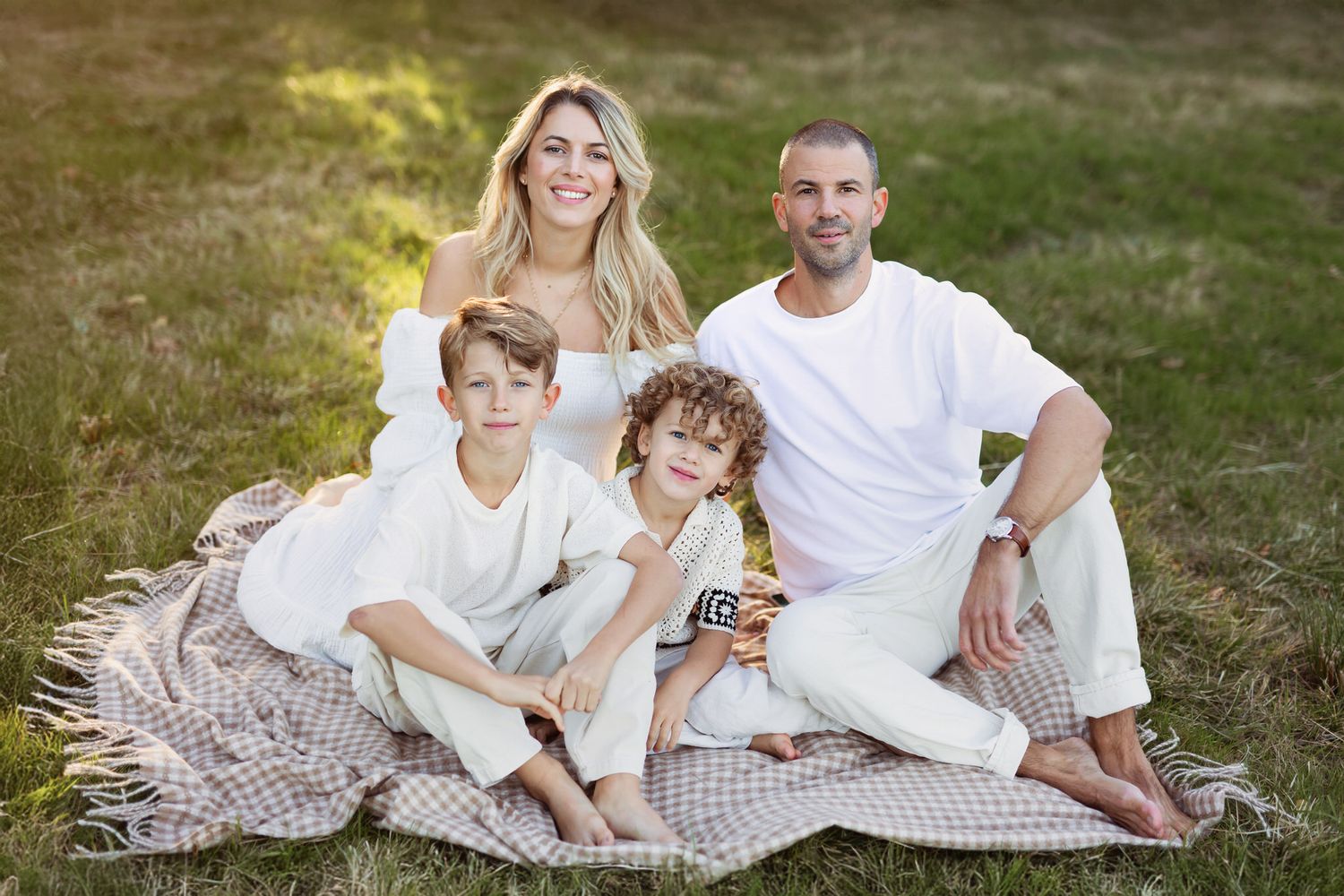 familjefotografering i Göteborg, sen sommar. mamma, pappa och två barn sitter på en filt och myser.