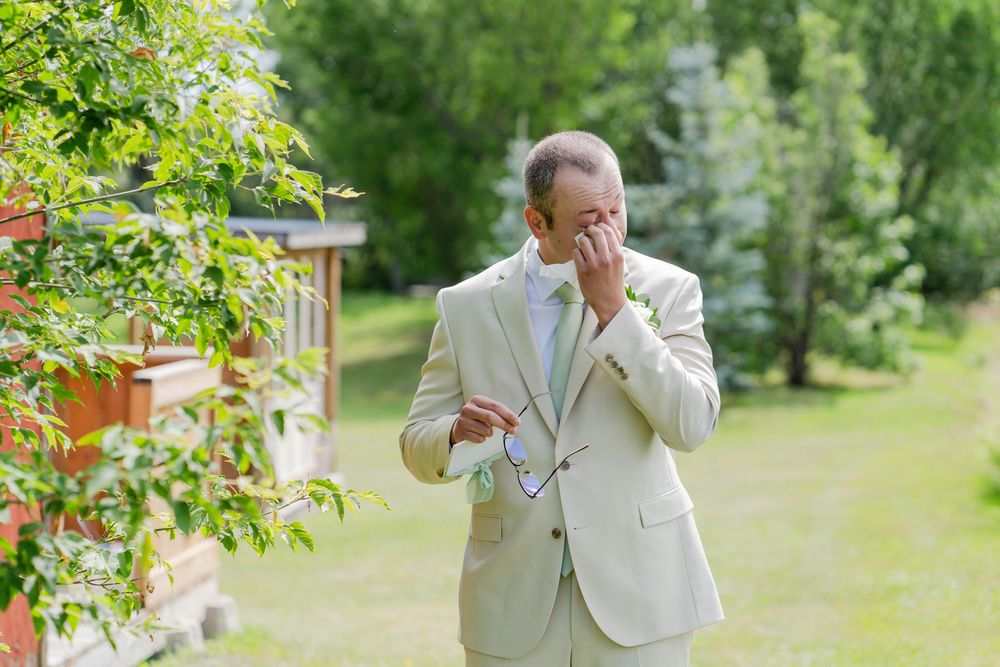 Someone in a light suit reacts emotionally during an outdoor photoshoot in a lush garden setting.