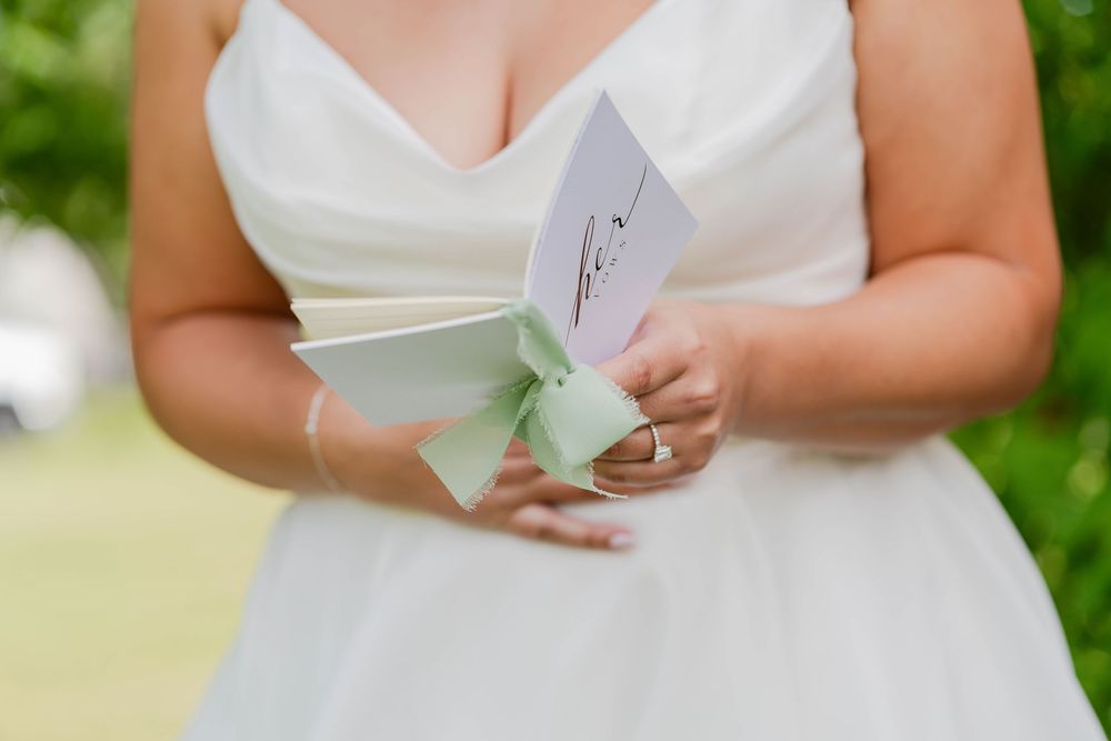 Close-up view of hands in a white dress holding a mint green and white wedding card or letter.