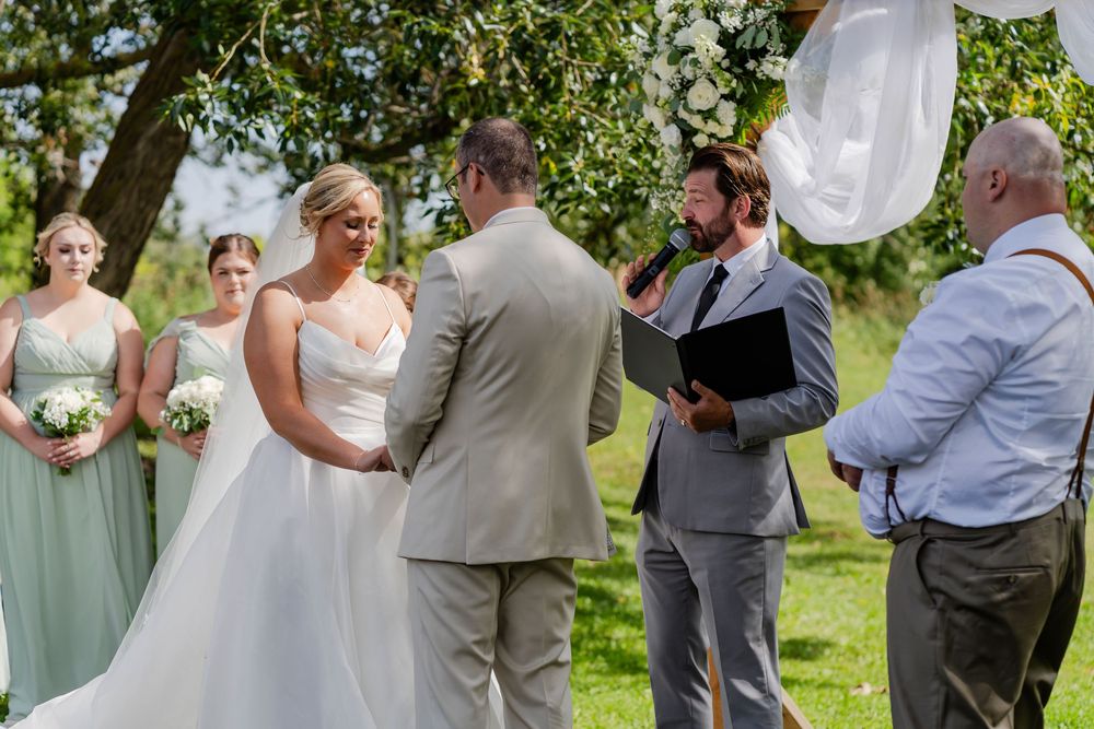Wedding party members laugh and celebrate together during outdoor summer celebration in a garden setting.