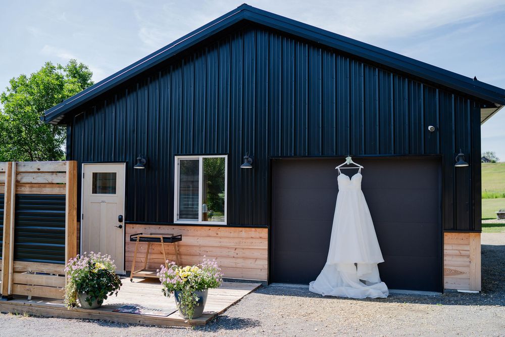A modern black and wood-sided exterior of a wedding venue with white wedding dresses displayed on outdoor walls.