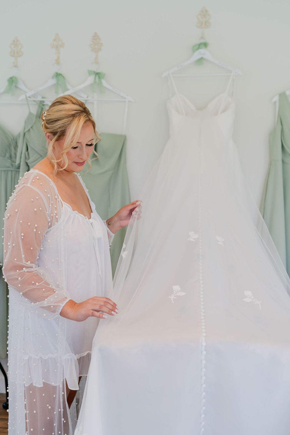 A bride in a sheer white robe examines elegant wedding dresses hanging on display in a bridal boutique.