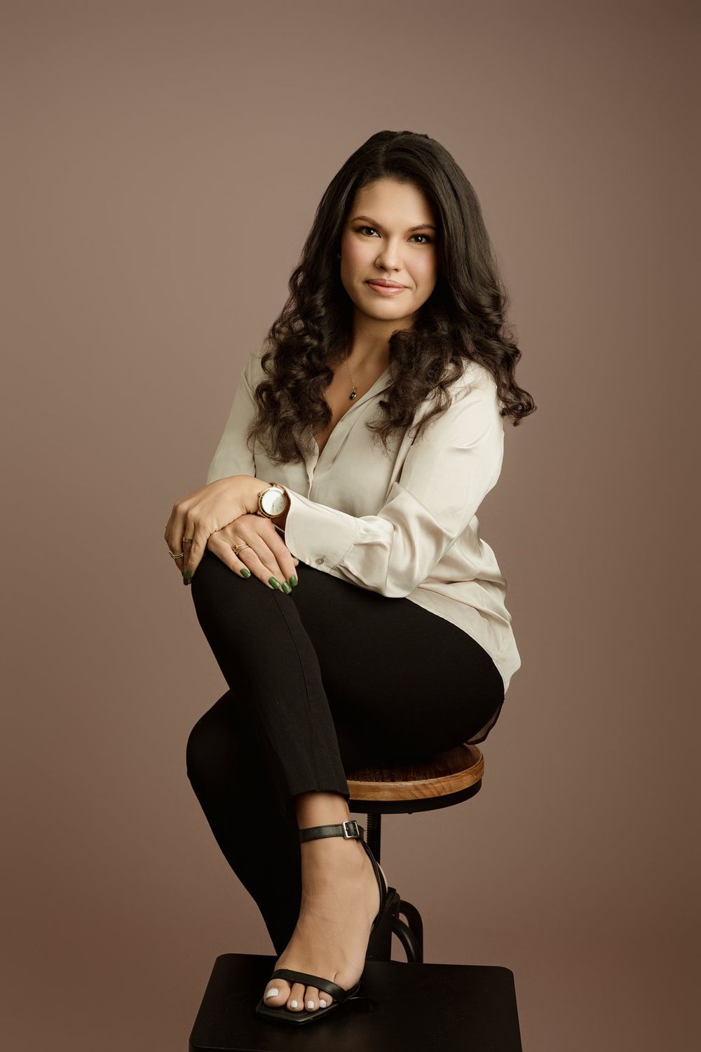 Professional Miami headshot of a seated woman against a warm neutral studio background.