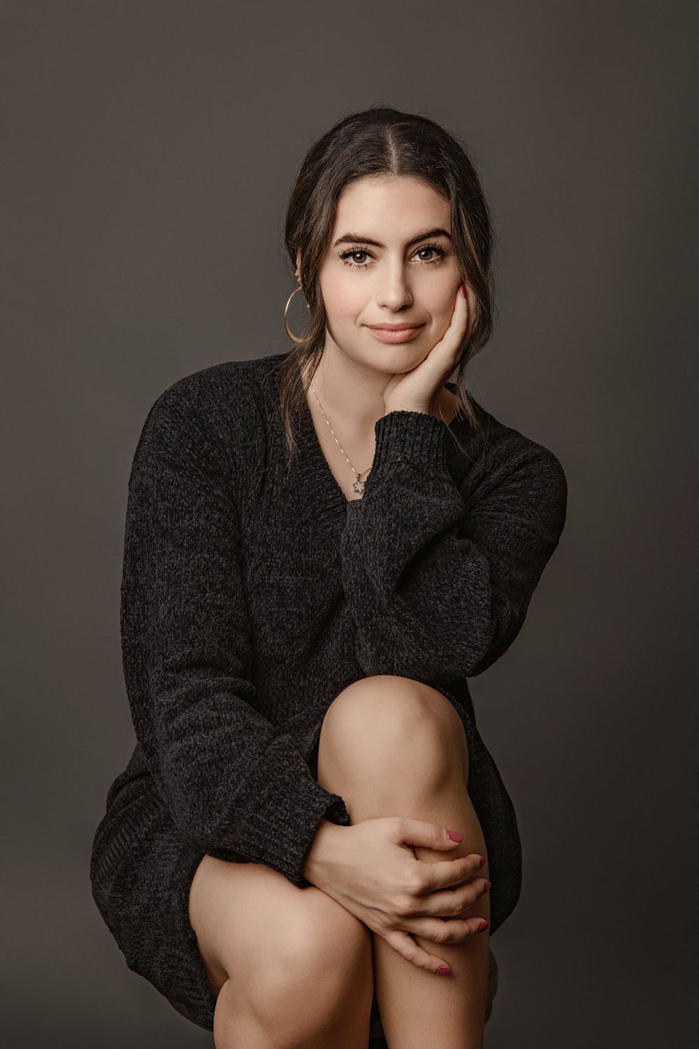 Professional Miami portrait of a woman in a black sweater against a dark neutral background.