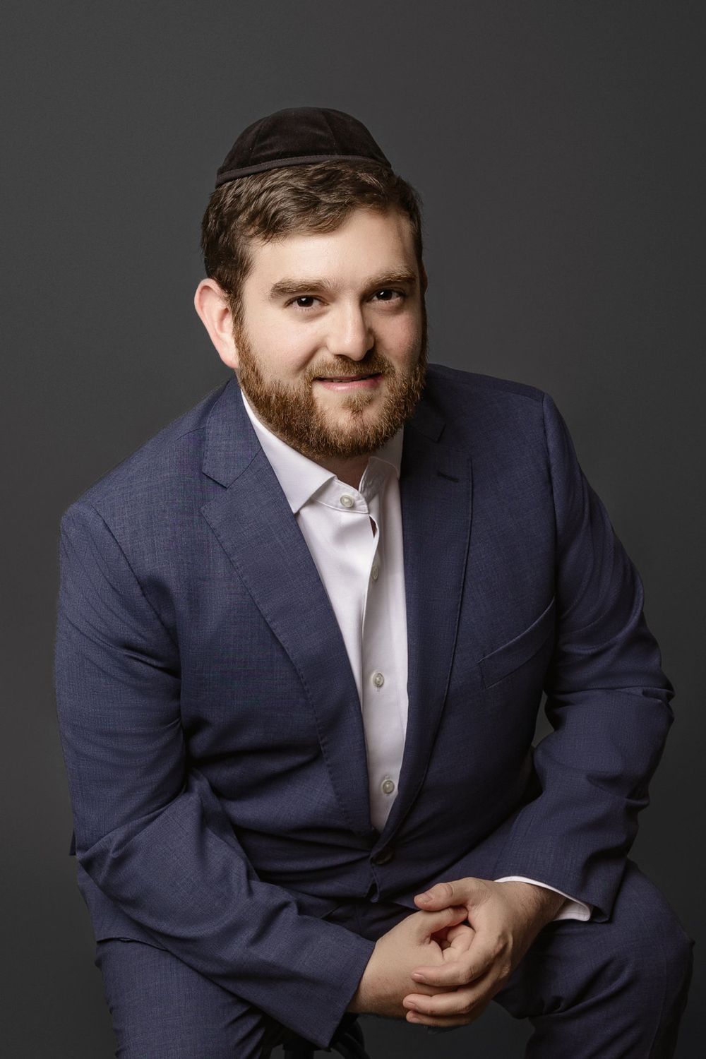 Professional Miami headshot of a bearded man in a blue suit against a charcoal studio background.
