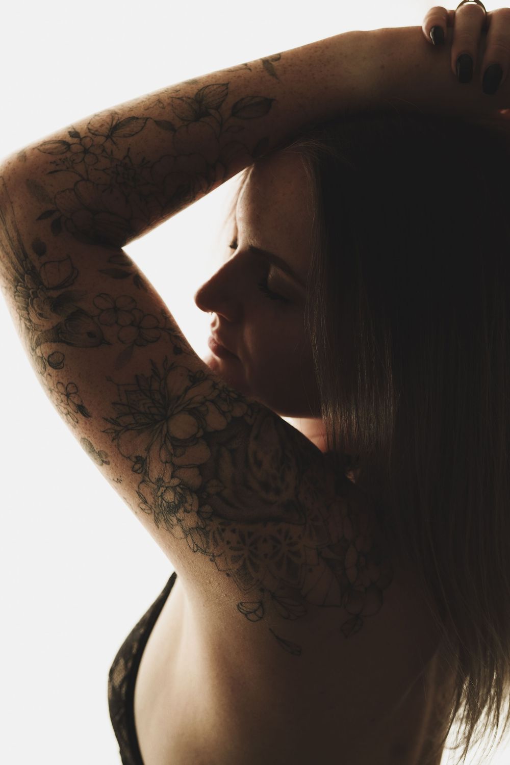 Woman with floral tattoo sleeve posing with arms raised, showcasing intricate black ink botanical designs on her arm.