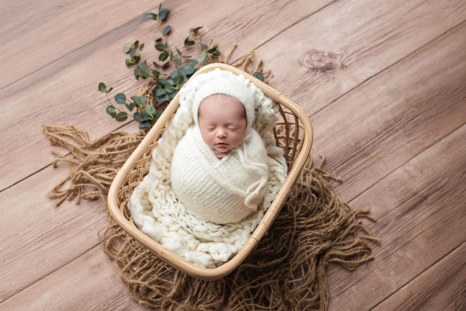 Sweet newborn pose with floral headband and angel wings against dark background.